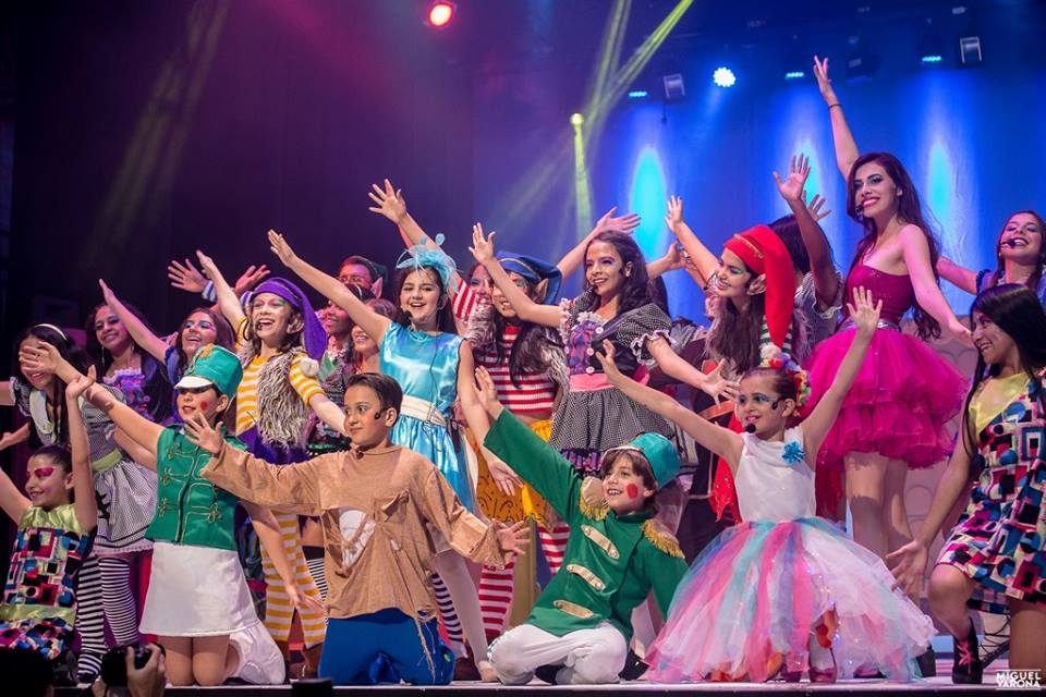 A large cast of children celebrating on stage, arms raised