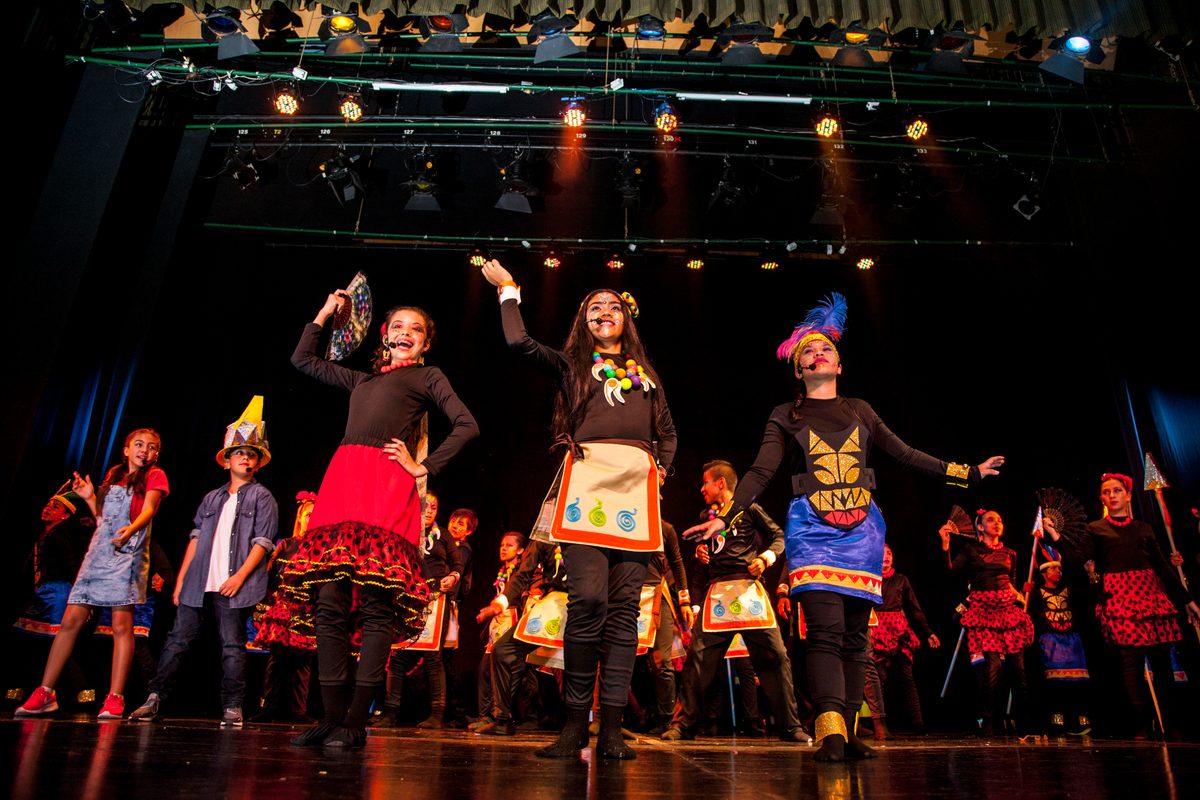 Three young performers in Indigenous-inspired costumes dance in front of the cast