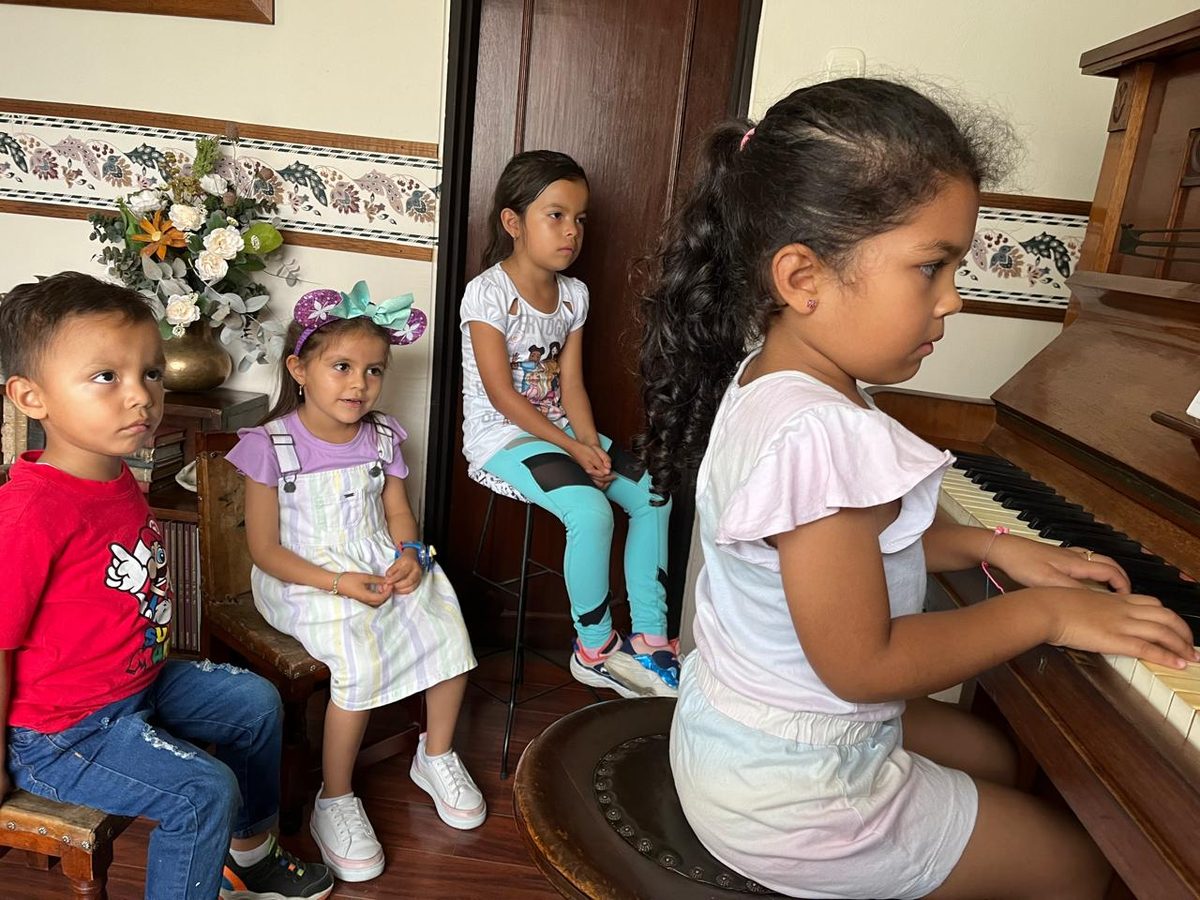 Young children gathered around a girl playing the piano