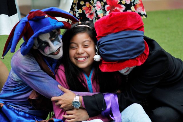 Un niño sonríe abrazado por dos actores con máscaras y sombreros