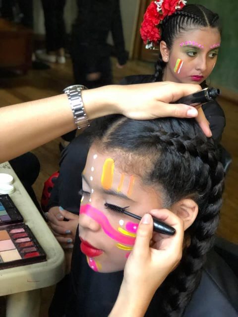 Una maquilladora pinta la cara de una niña con trenzas antes de la función