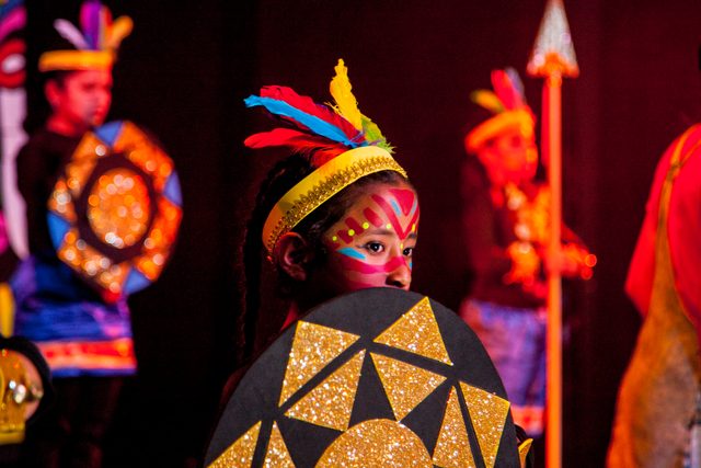 Un niño con tocado de plumas, escudo de colores y la cara pintada
