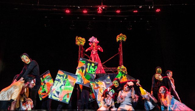 El elenco en escena con estandartes de colores y tótems
