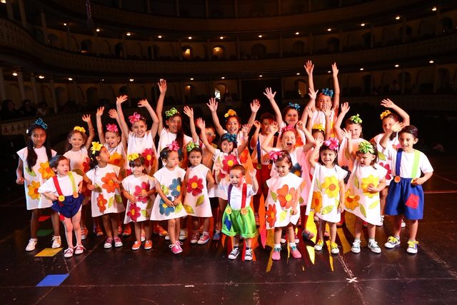 Coro infantil con los brazos en alto en un teatro