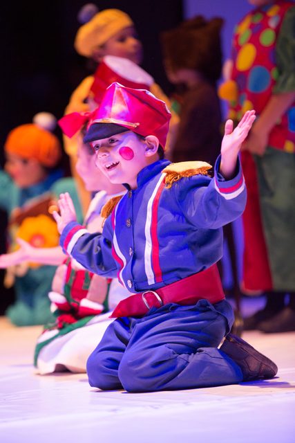Niño con vestuario de juguete, arrodillado en escena