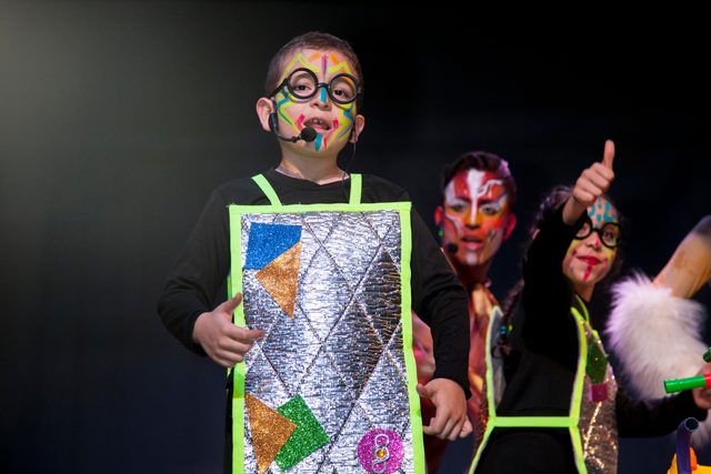Un niño con gafas, la cara pintada y traje plateado mira a la cámara