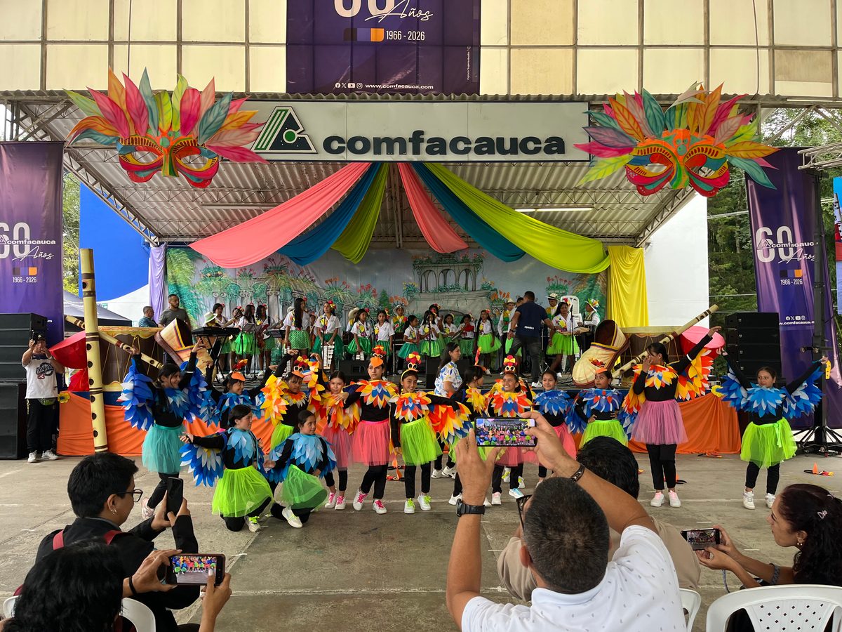 Children in bird costumes dance on the Comfacauca stage as the audience takes photos