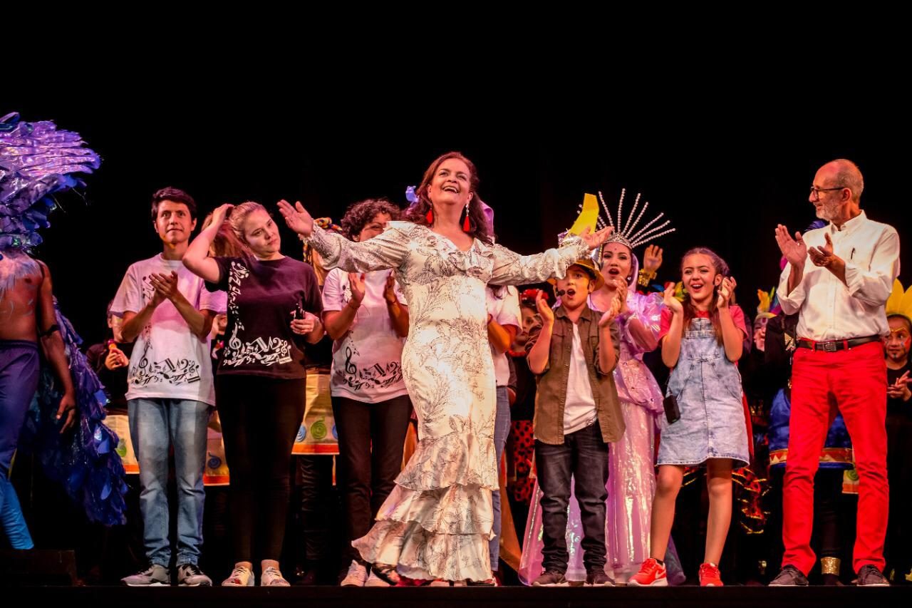 Rosana, in a white dress, applauds on stage with the cast at the end of a show